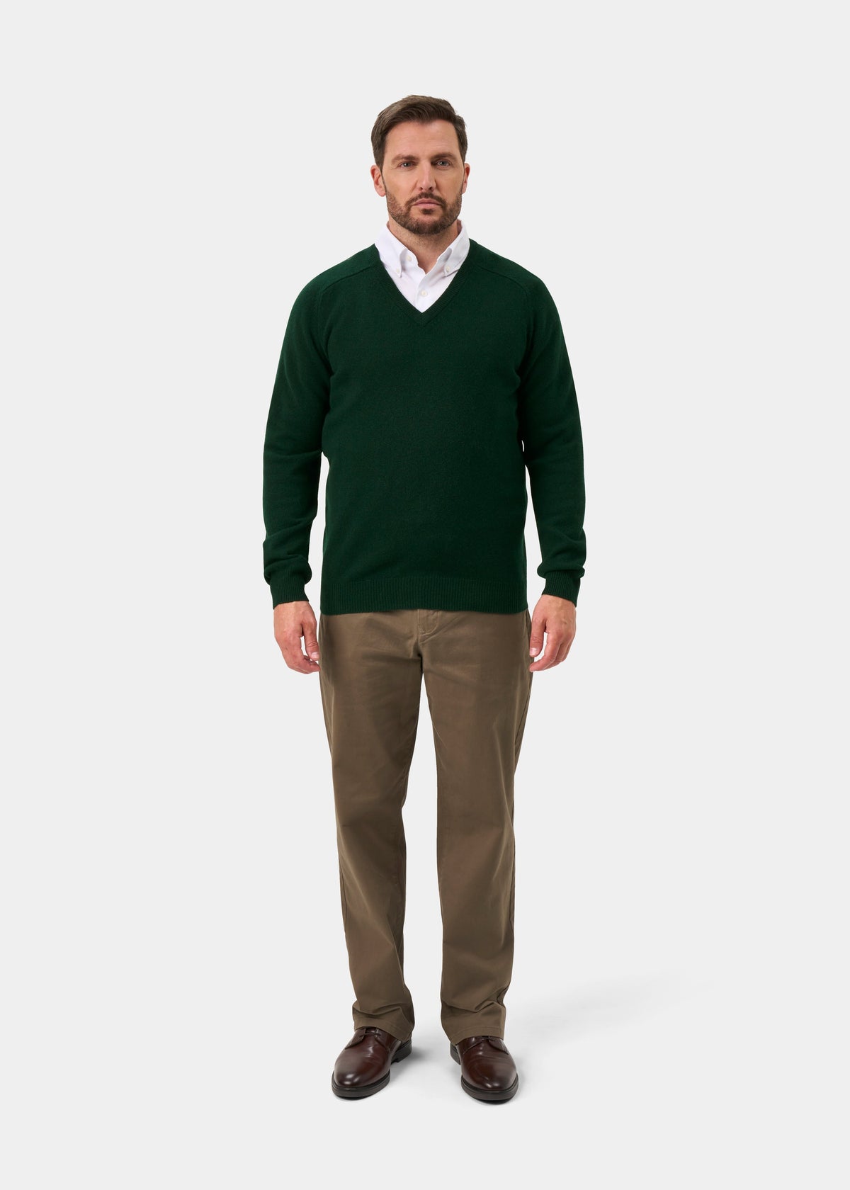Man in a Kilsyth Lambswool V-Neck Jumper in Mallard, white shirt, khaki pants & brown shoes on a plain white background.