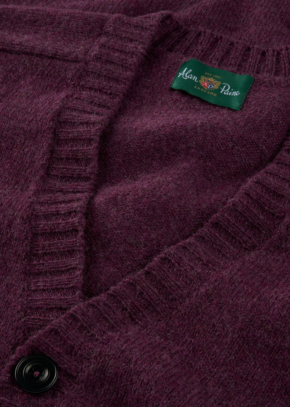 Close-up of the Kinloch Supersoft Shetland Wool V-Neck Cardigan in Elderberry with black button and green label.