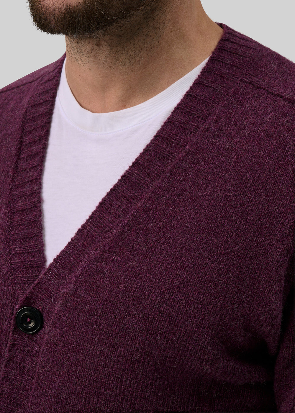 A person wears a white T-shirt and a Kinloch Supersoft Shetland Wool V-Neck Cardigan in Elderberry.