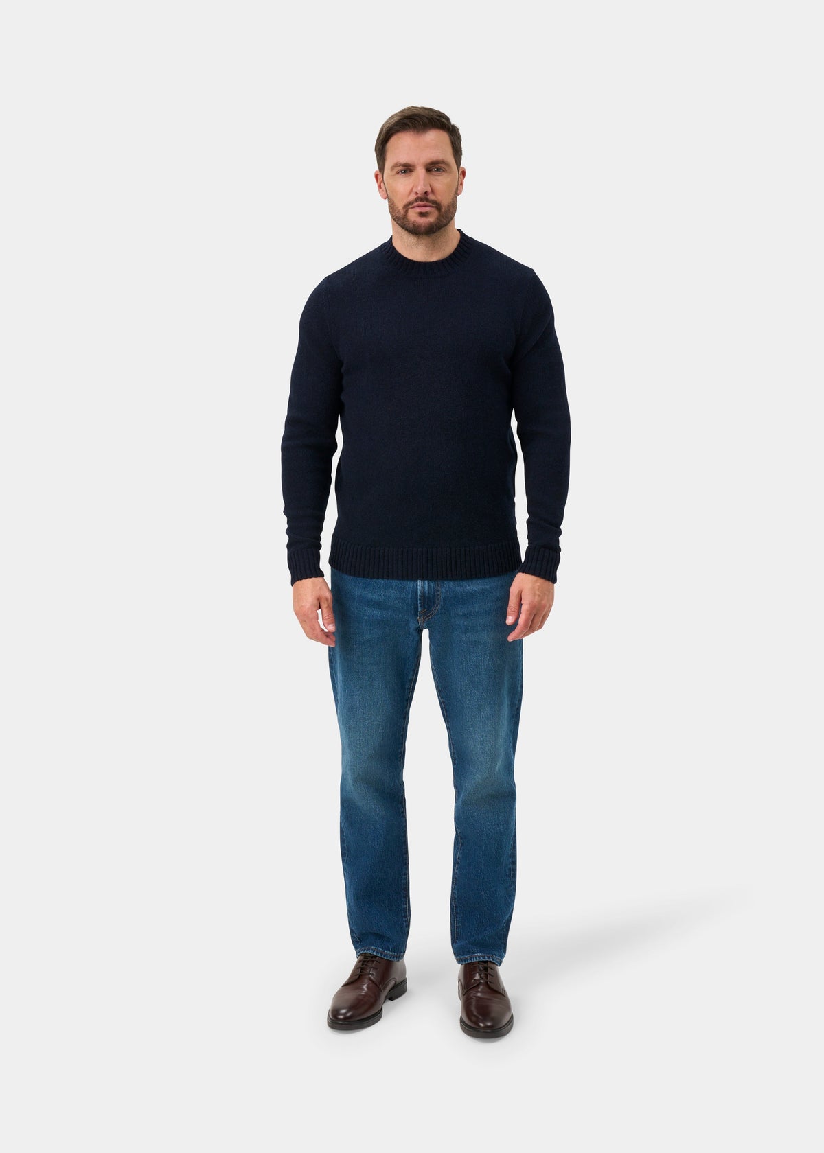 Man in a Kinnadie Supersoft Shetland Wool Crew Neck Jumper (Concord), blue jeans, brown shoes, on white backdrop.