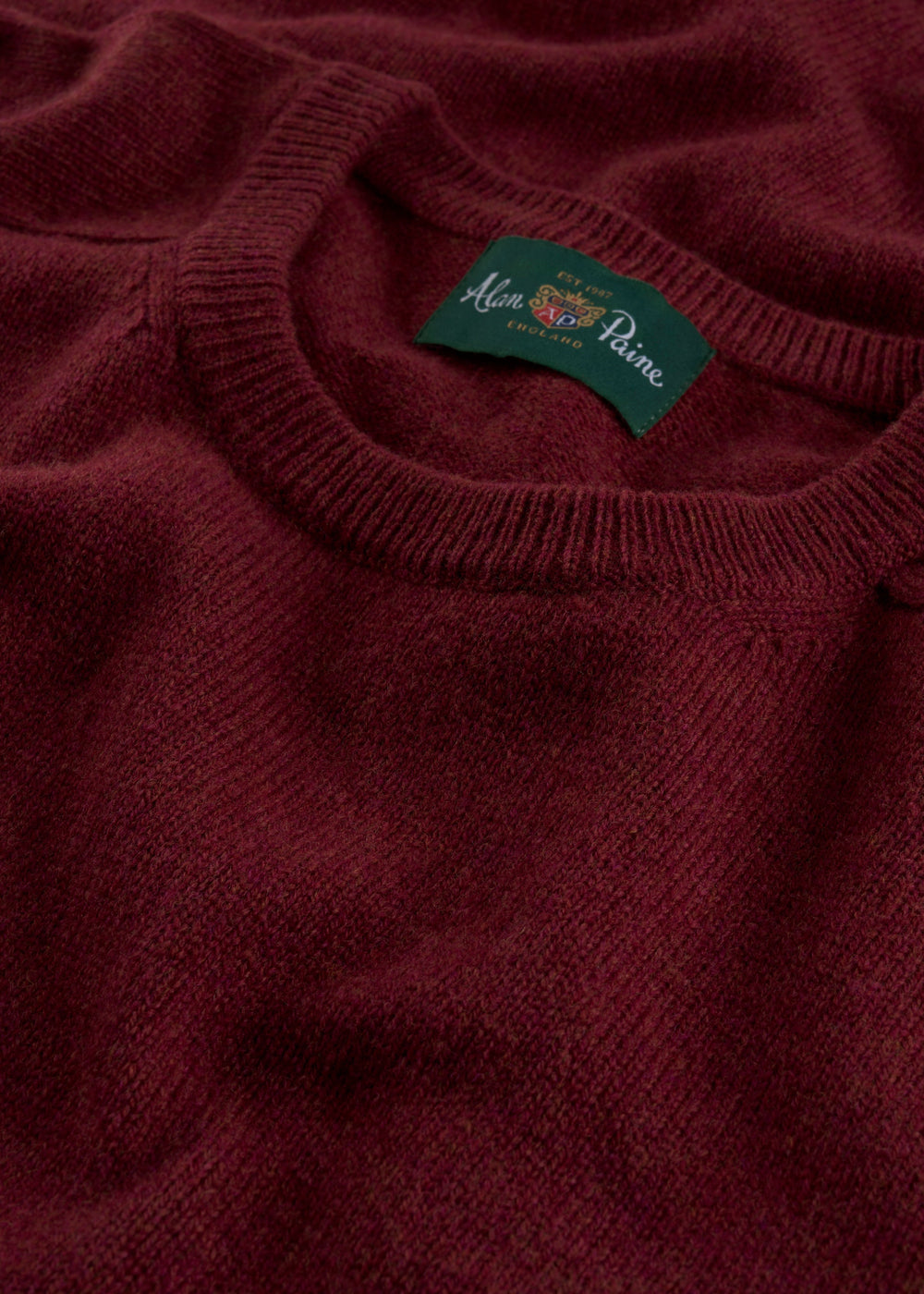Close-up of the Lenzie Lambswool Crew Neck Jumper in garnet with the Alan Paine England label on the collar.