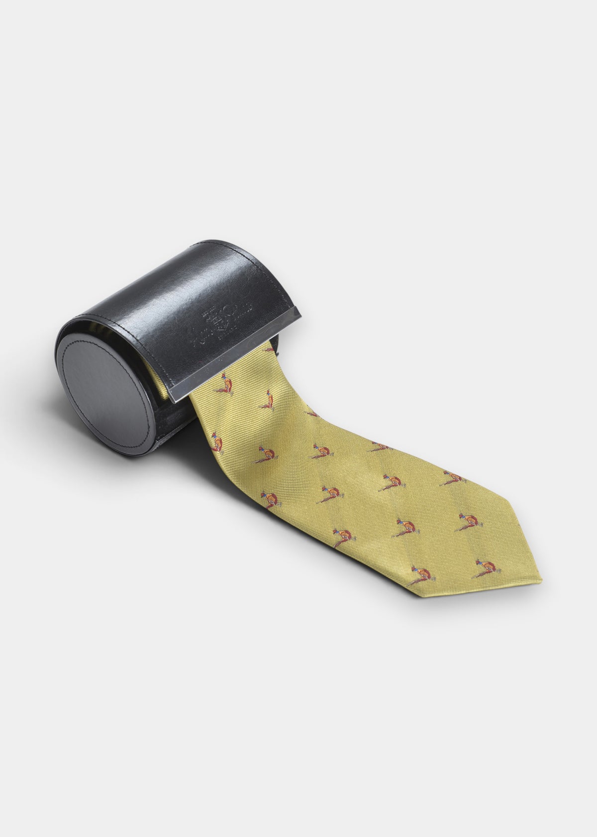 Ripon Silk Country Tie In Gold - Standing Pheasant Design partially rolled inside a dark cylindrical case.