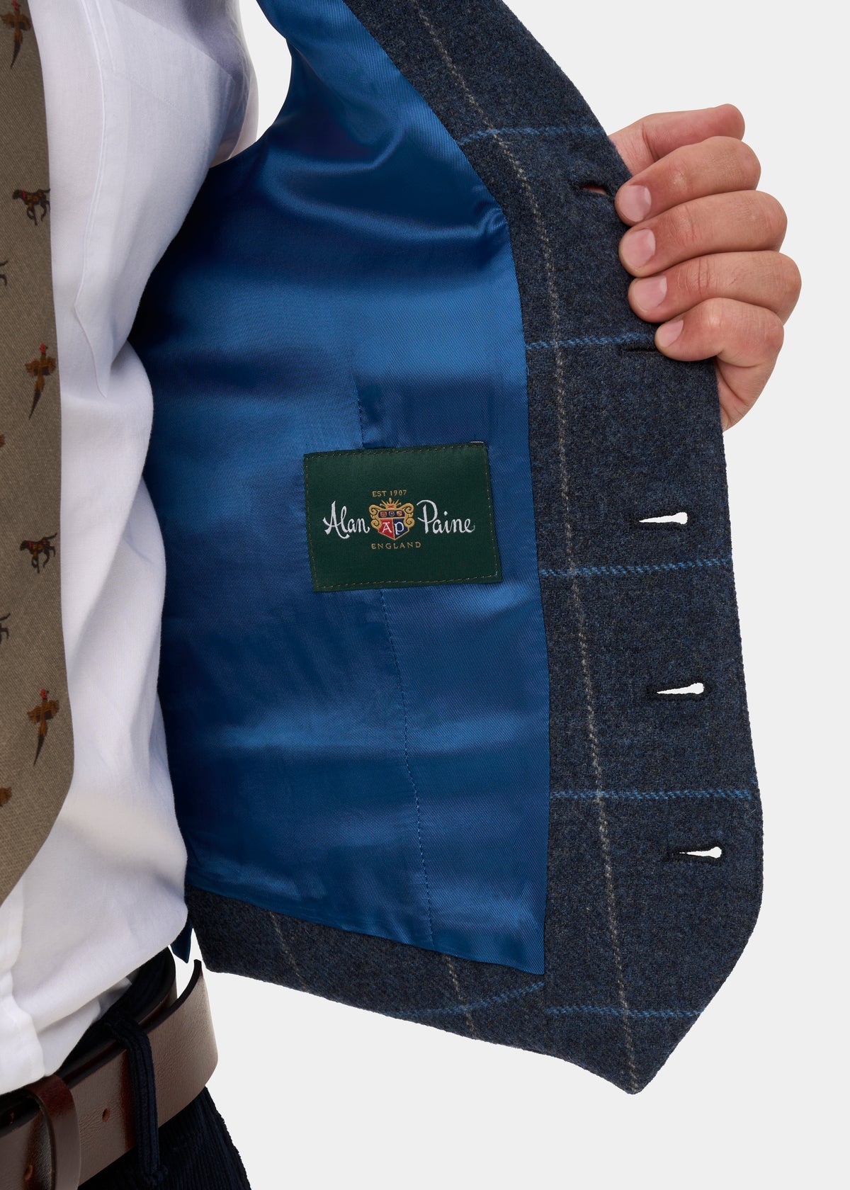 Hand holding open a Surrey Men’s Tweed Water Repellent Lined Waistcoat in Midnight Blue to show its lining and brand label.