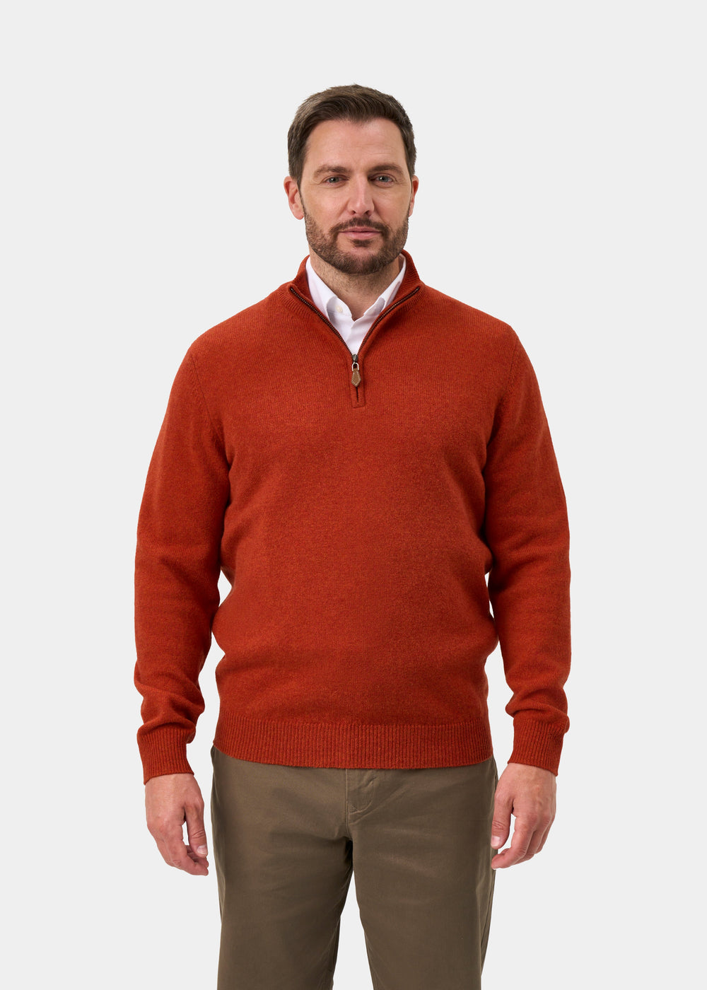 A man wears a Sutherland Lambswool Quarter Zip Jumper In Ember over a white collared shirt and olive trousers.