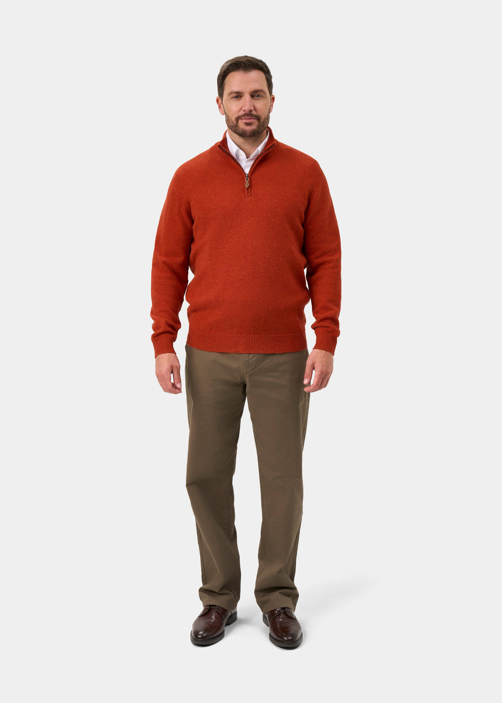 A man wears a Sutherland Lambswool Quarter Zip Jumper In Ember over a white shirt, brown trousers, and dark shoes.