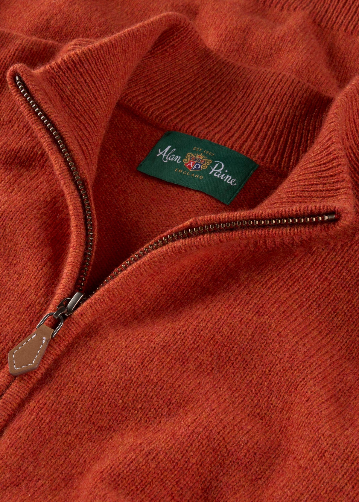 Close-up of a rust-orange Sutherland Lambswool Quarter Zip Jumper In Ember, showing the zippered collar and inner label.