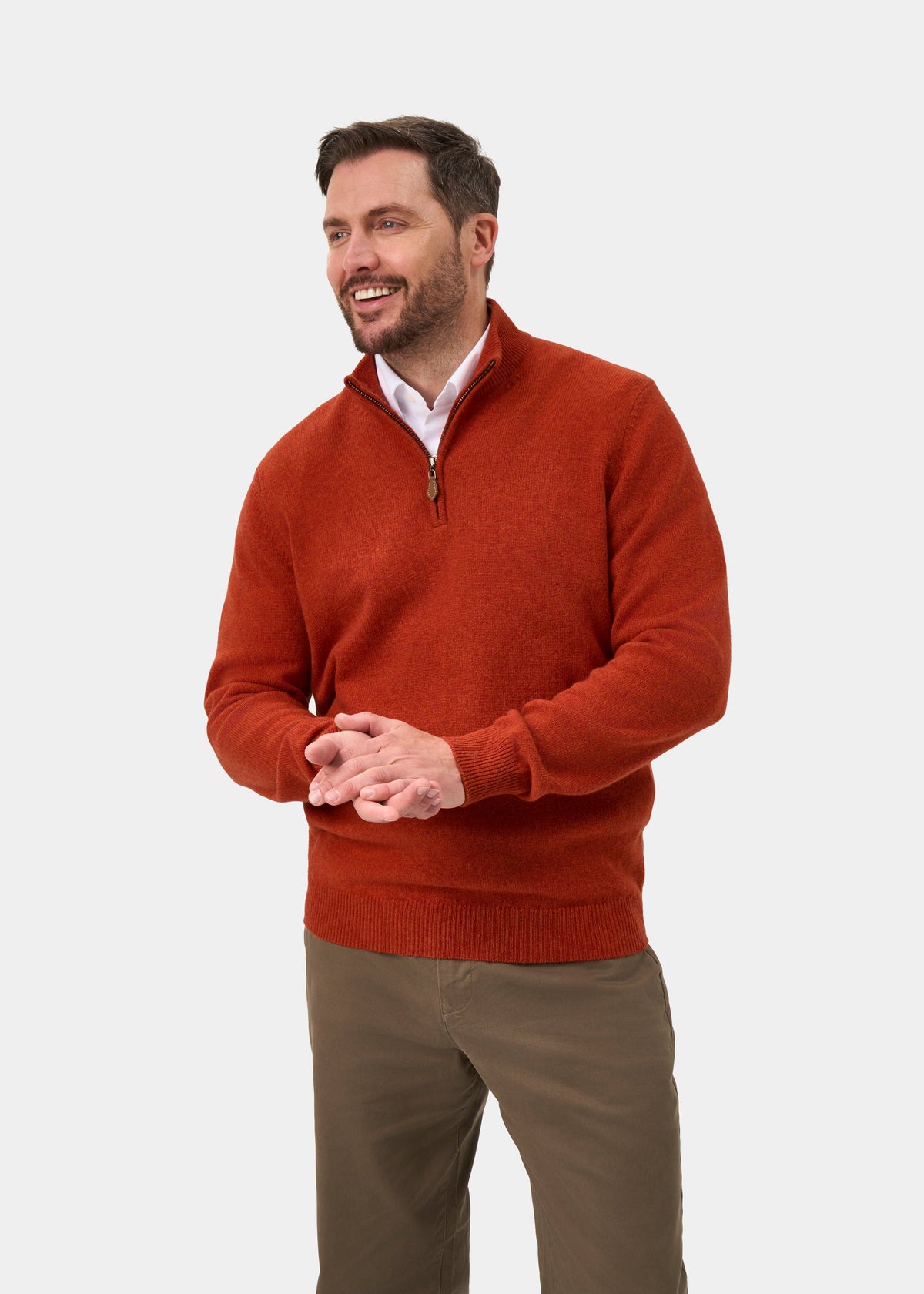 A smiling man wearing a Sutherland Lambswool Quarter Zip Jumper In Ember over a white collared shirt and brown trousers.