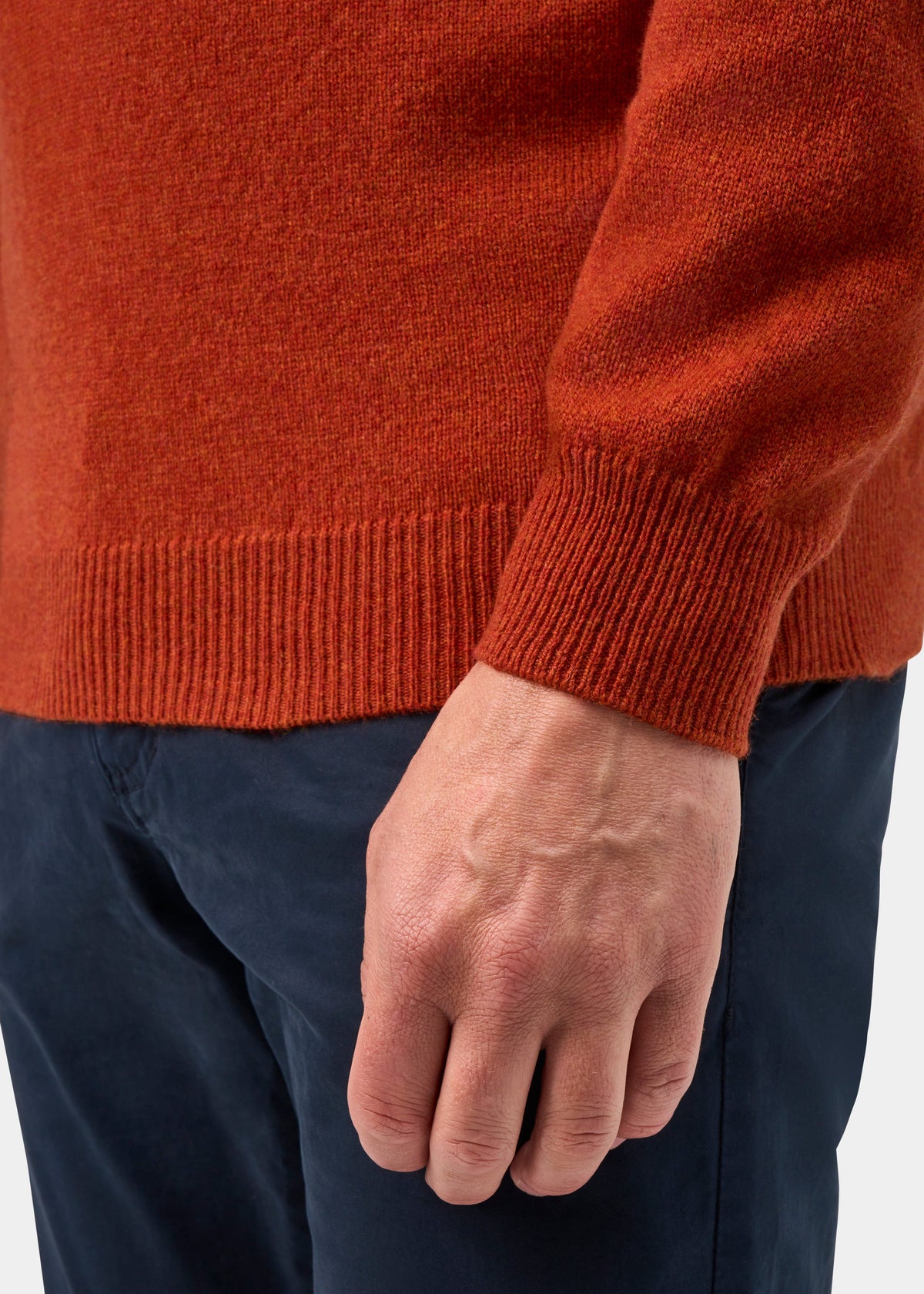 Close-up of a rusty orange Sutherland Lambswool Quarter Zip Jumper In Ember with a ribbed hem worn over navy trousers.