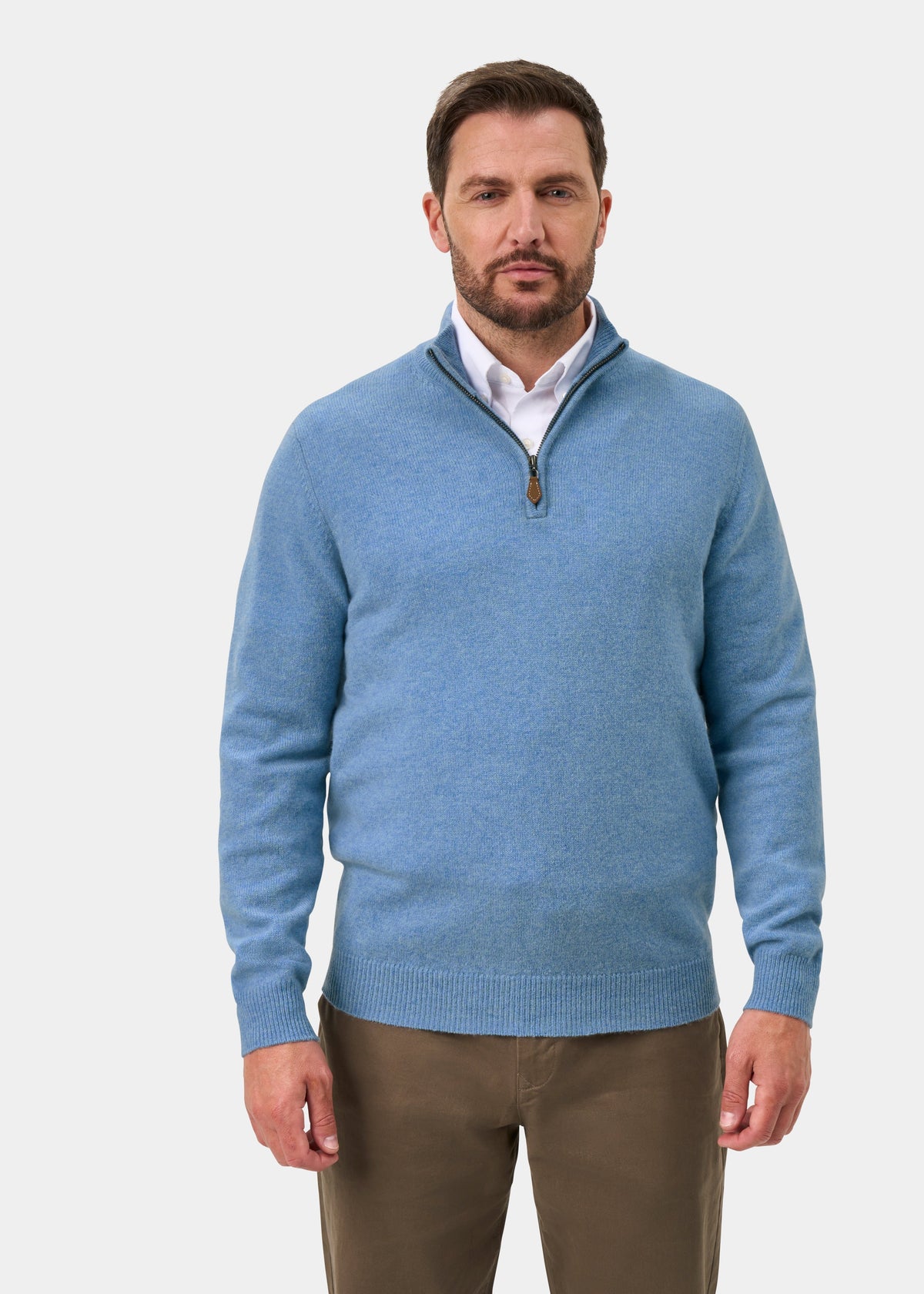 A man wearing a Sutherland Lambswool Quarter Zip Jumper In Glacier over a white collared shirt and brown trousers.