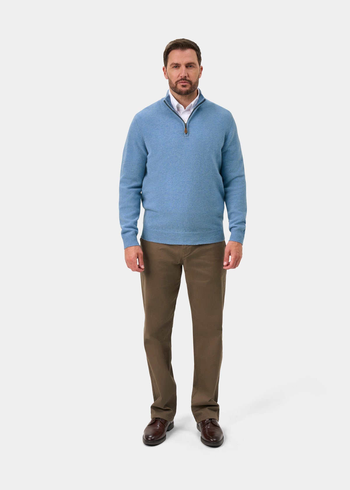 Man in a Sutherland Lambswool Quarter Zip Jumper In Glacier worn over a white collared shirt and brown trousers.