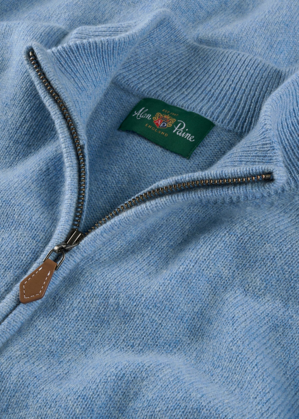 Sutherland Lambswool Quarter Zip Jumper in Glacier, a light blue sweater with a metal zipper and branded green neck label.