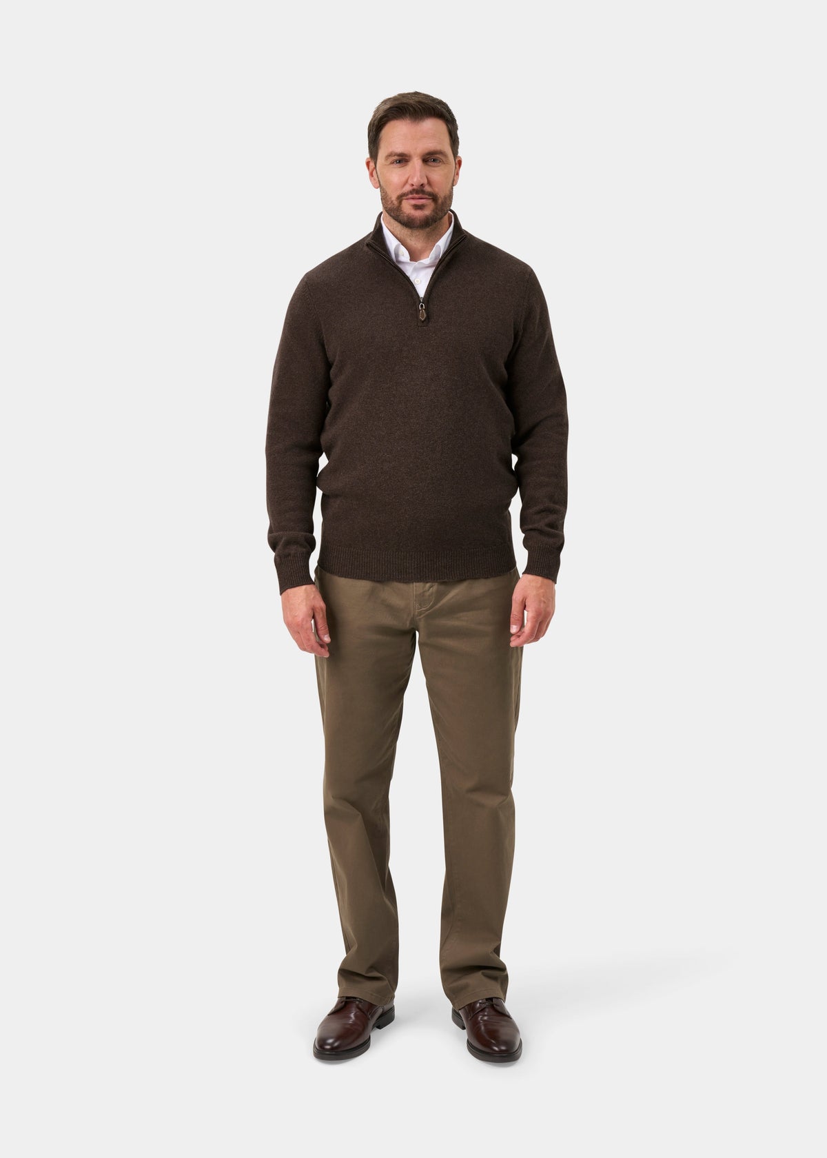 A man wearing a Sutherland Lambswool Quarter Zip Jumper In Mocha over a white shirt, olive trousers, and dark brown shoes.