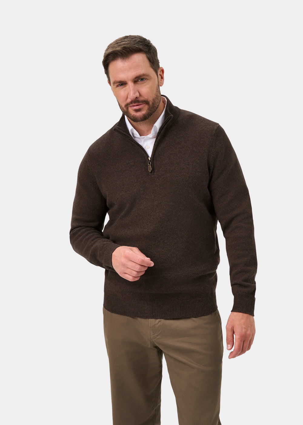 A man wears a Sutherland Lambswool Quarter Zip Jumper In Mocha over a white collared shirt with brown trousers.